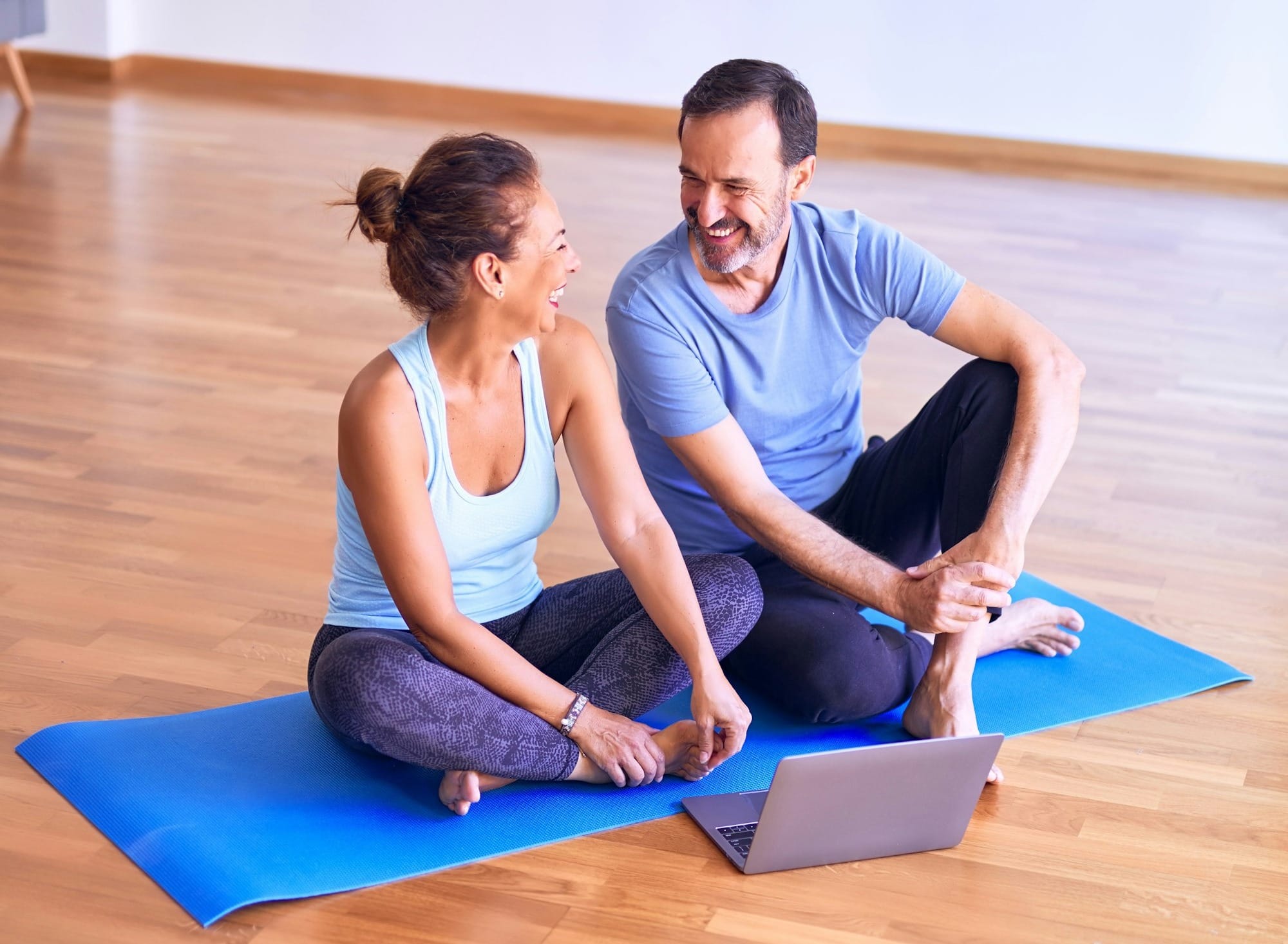 Middle age beautiful sporty couple smiling happy. Sitting on mat with smile on face using laptop at gym